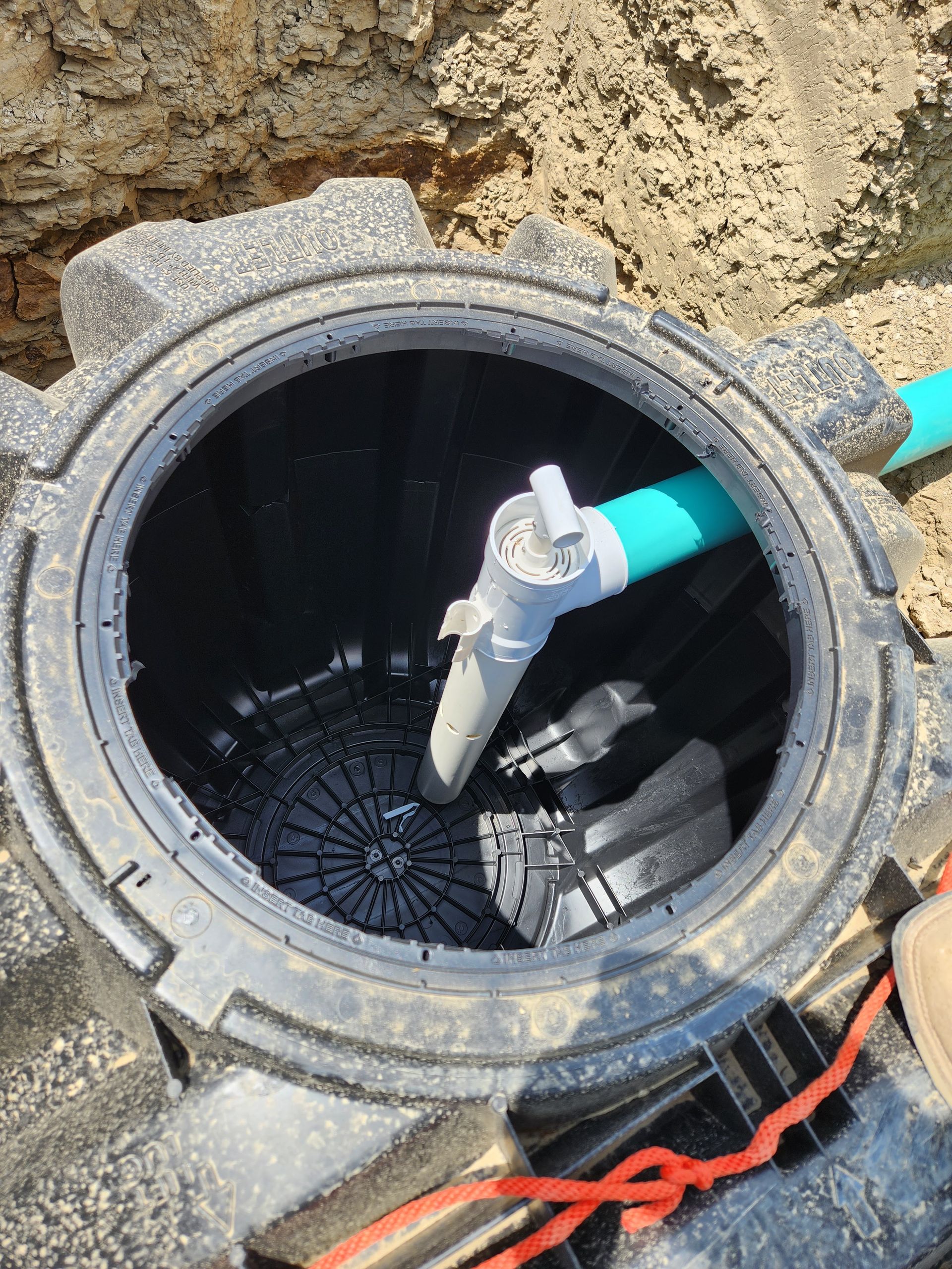 Open septic tank with a blue pipe and a white valve, set in a dirt excavation.