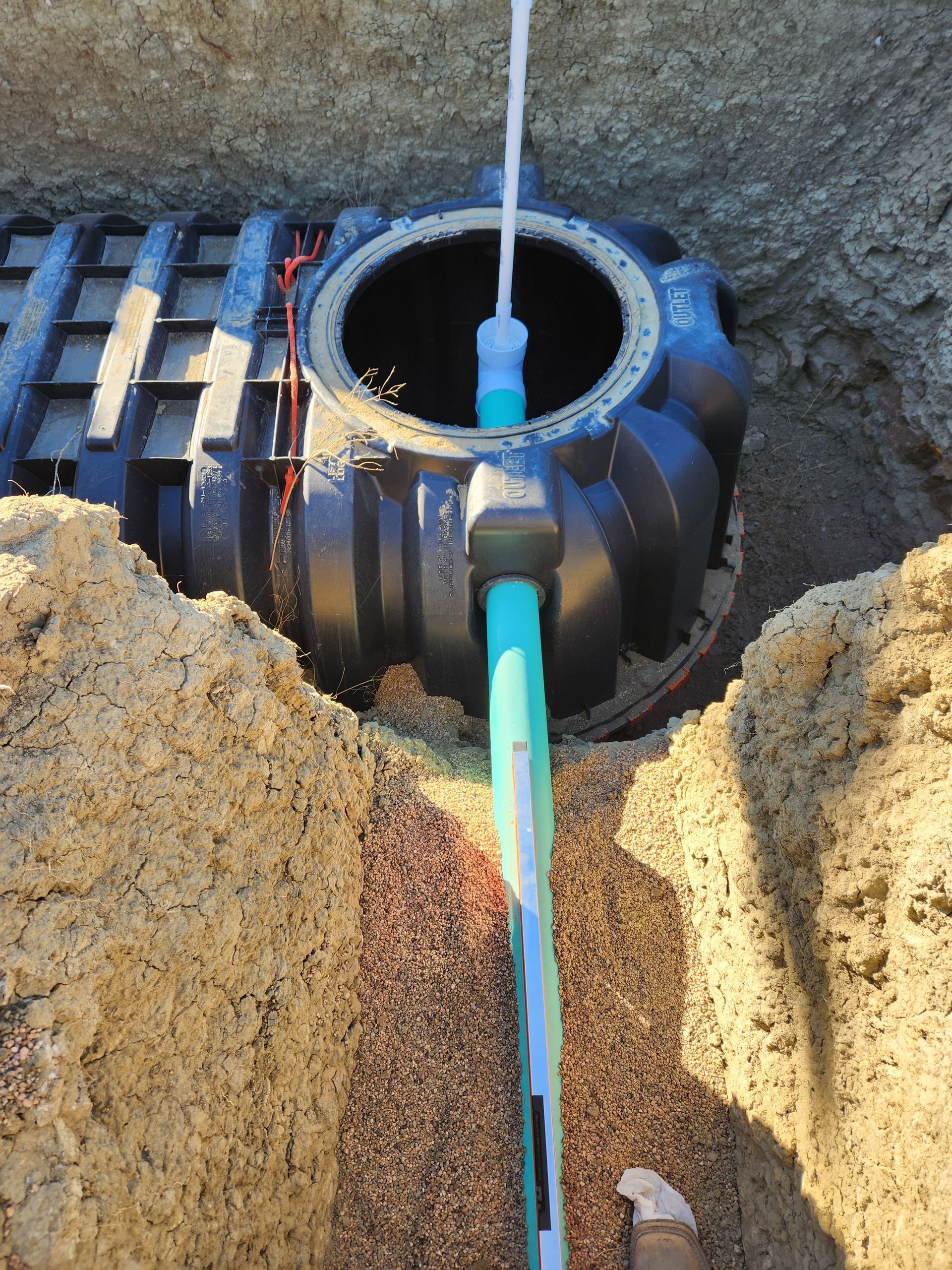 Open septic tank with water being poured in, surrounded by dirt and gravel.
