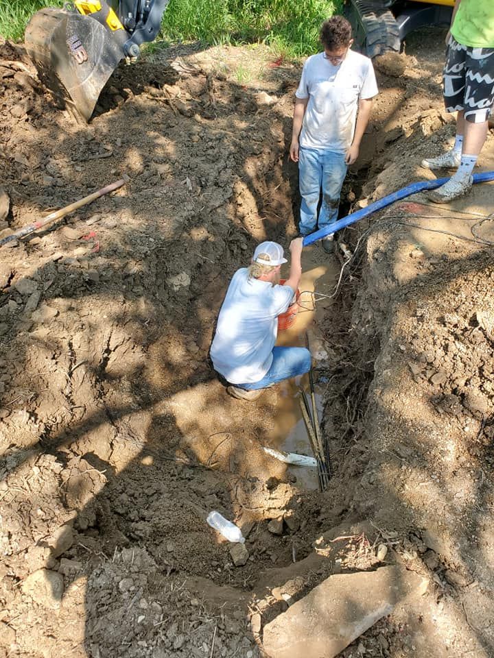 Men working in a trench with pipes; outdoor setting with heavy equipment.