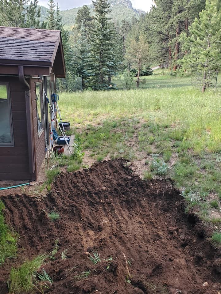 A house with a small excavated area in the yard, ready for planting, with a mountain backdrop.