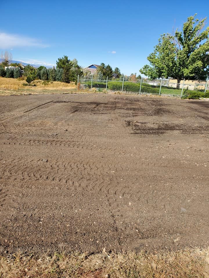 Brown soil, likely tilled, in an open field, with fence and trees in background under a blue sky.