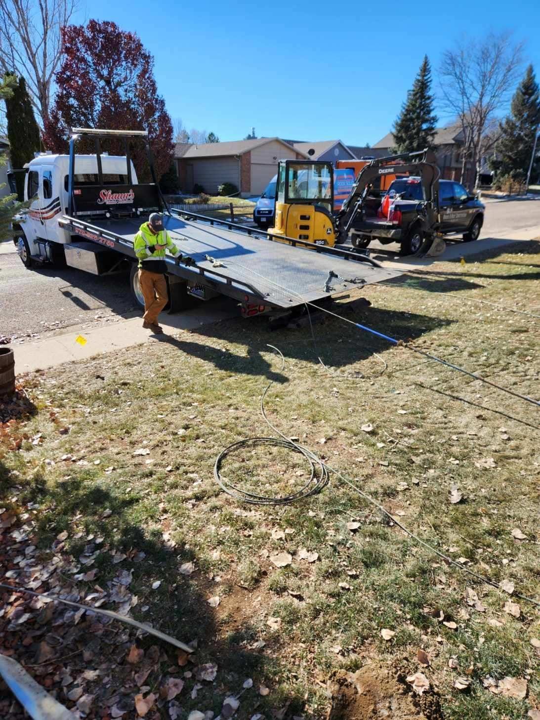 Tow truck operator prepares to load a vehicle and mini excavator on a sunny day.
