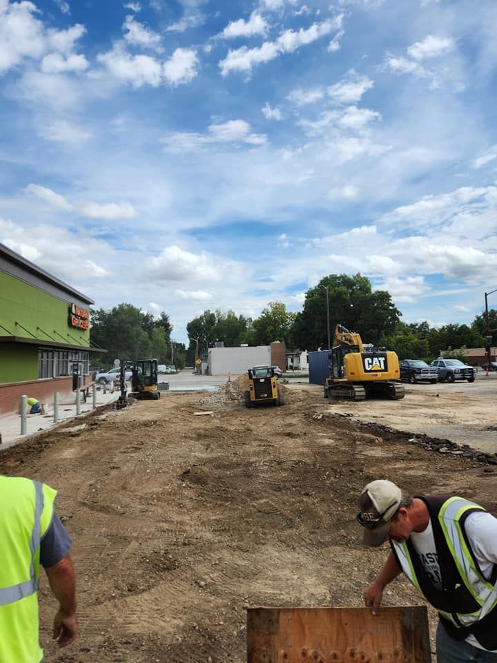 Construction site with heavy machinery, workers, and building under a cloudy sky.
