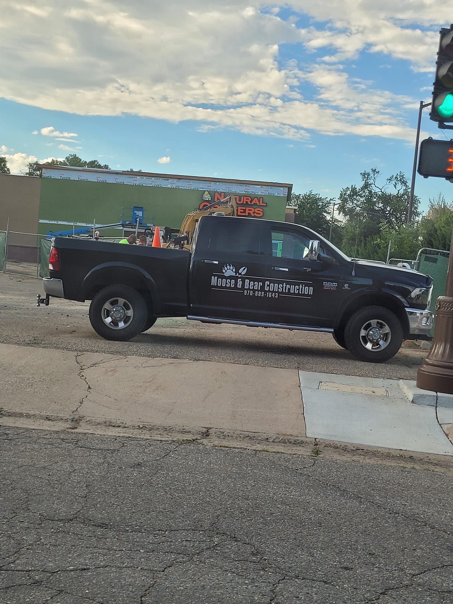 Black pickup truck parked next to a curb and traffic light. Building and sky in the background.