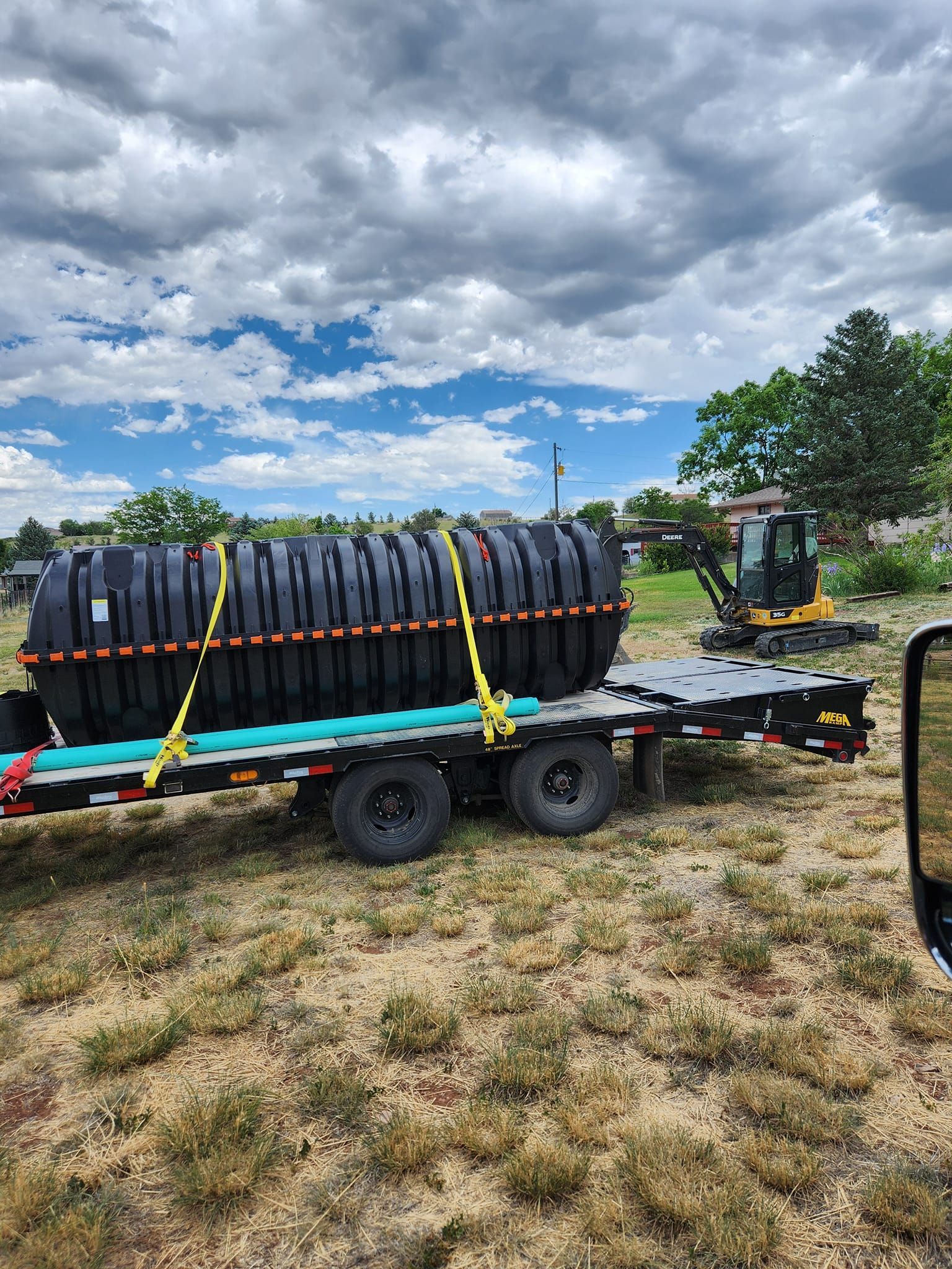 A black septic tank strapped to a trailer in a grassy area with a cloudy sky.