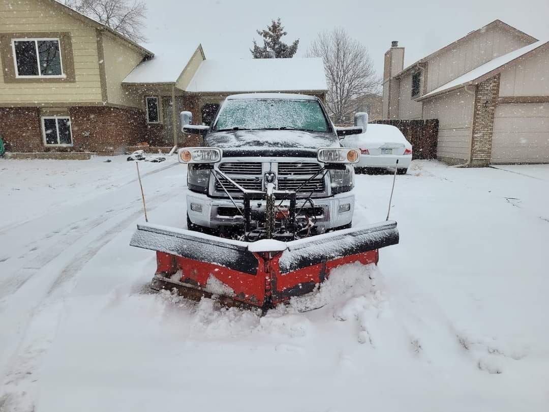 Snowplow clearing a snow-covered residential driveway during a winter storm.