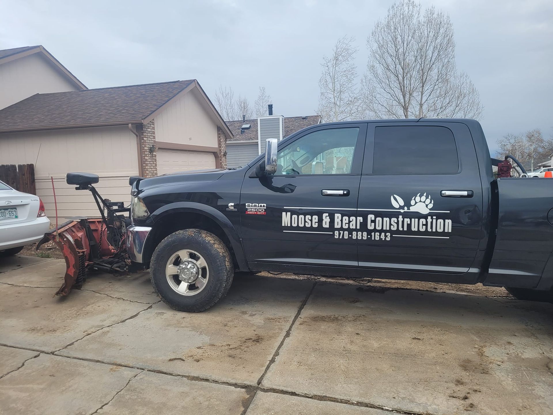 Black Moose & Bear Construction truck with snowplow parked in a driveway.