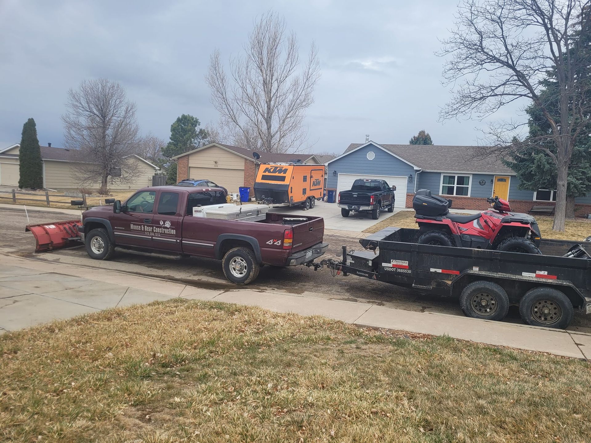 Burgundy truck towing a trailer with an ATV parked in a suburban driveway on a cloudy day.