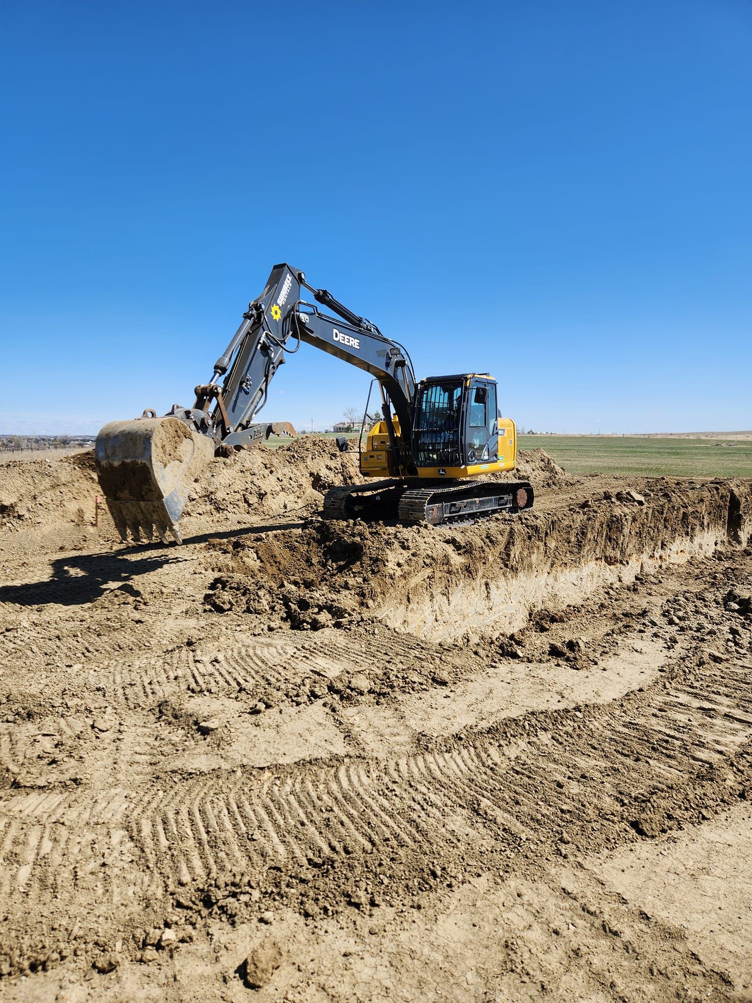 Excavator digging a trench in a brown dirt field under a clear blue sky.