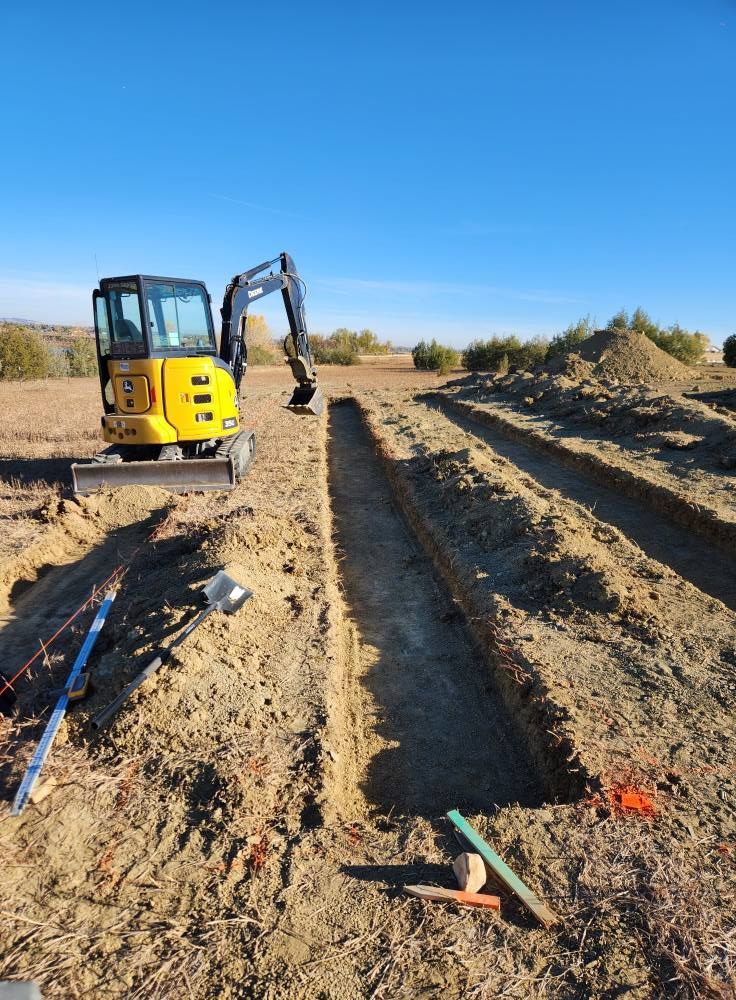 Yellow excavator digging trenches in a field under a clear, blue sky.
