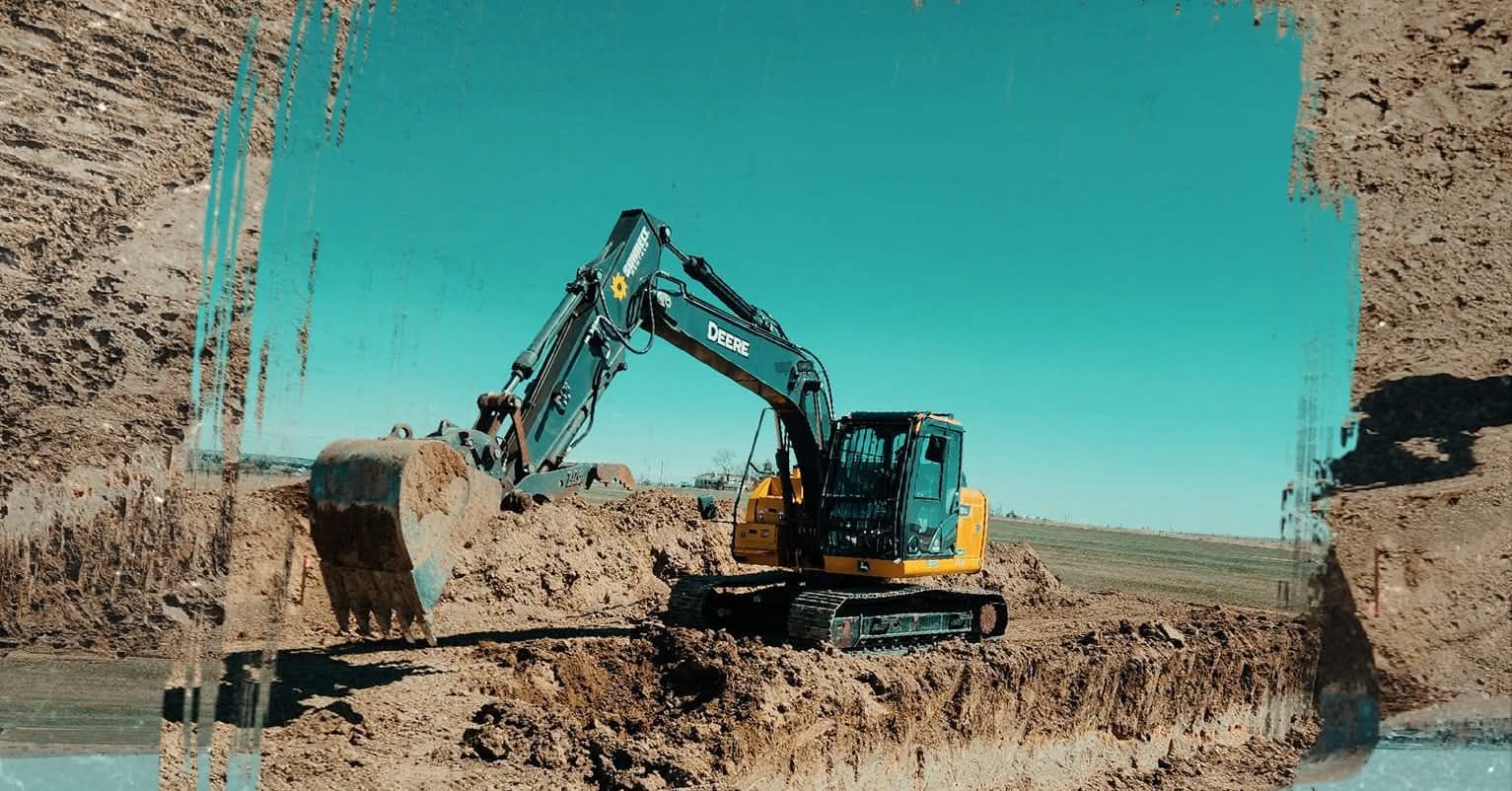 Excavator digs into a mound of dirt under a bright blue sky.