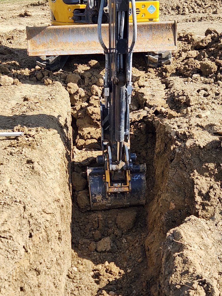 Mini excavator digging a trench in brown soil on a sunny day.