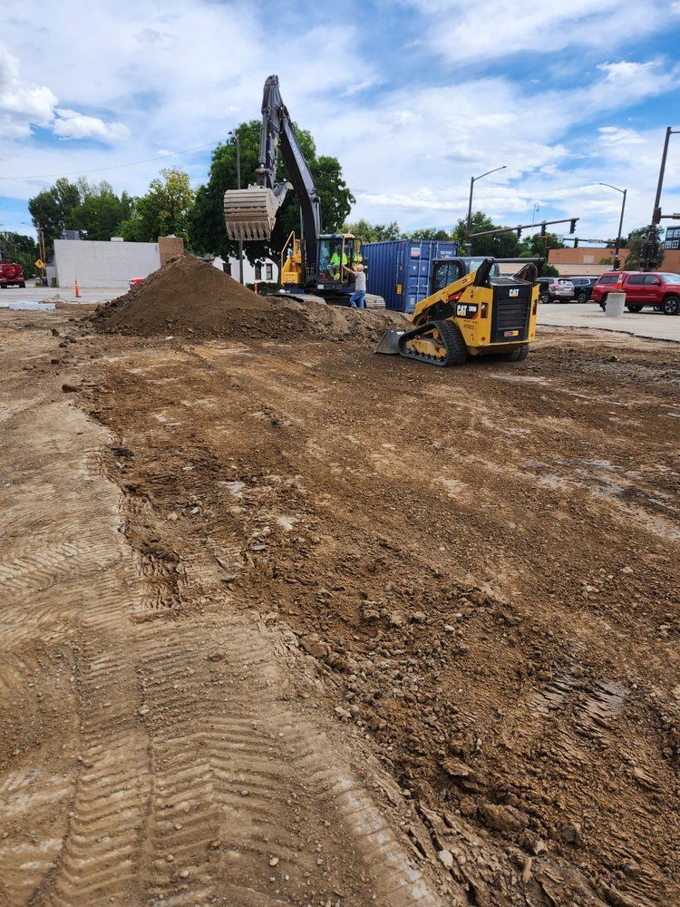 Construction site with an excavator and skid steer, moving dirt under a cloudy sky.