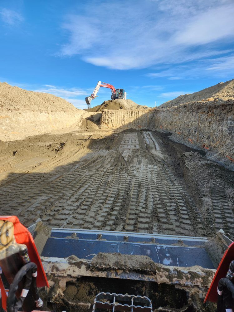 Excavator works on a dirt ramp, another excavator in the background, blue sky.