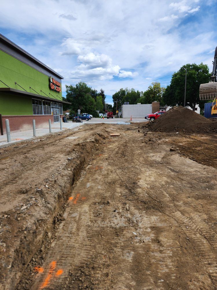 Trench dug in dirt, likely for construction, in front of a green-sided building on a sunny day.