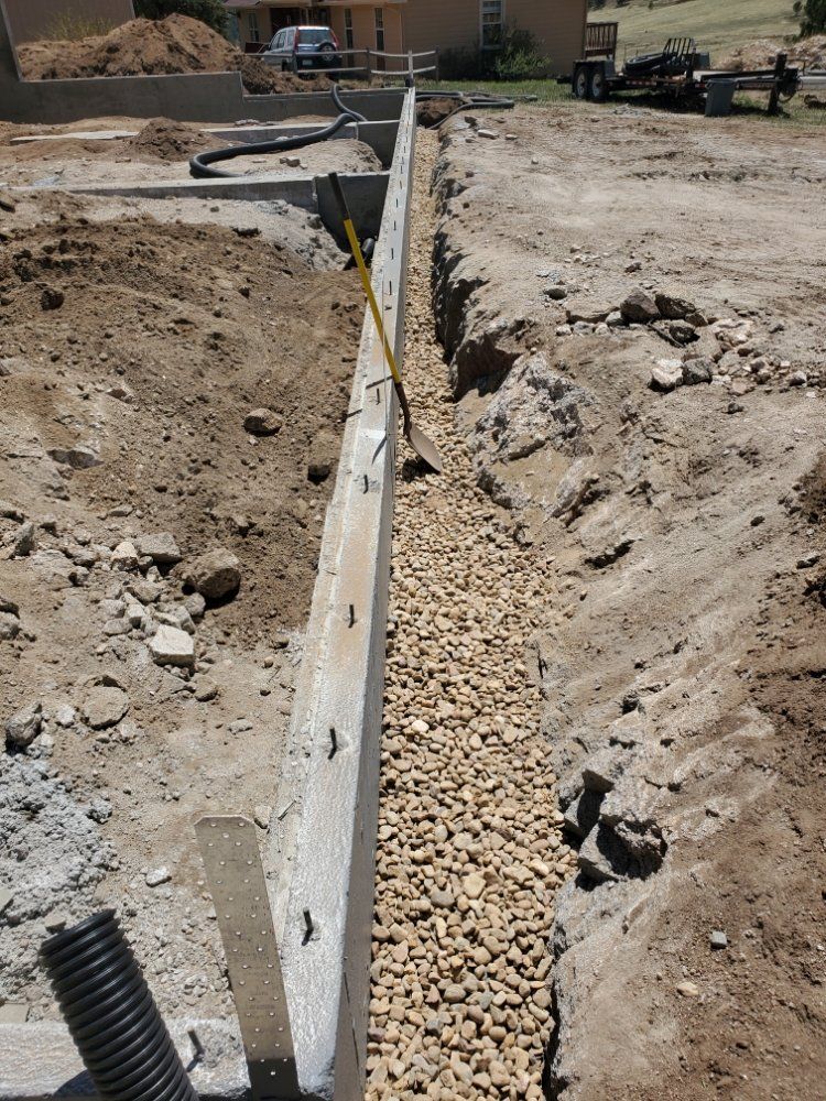 Construction site trench with gravel, concrete formwork, and corrugated pipe.