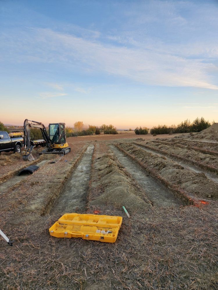 Trenches dug in a field with construction equipment and tools; a yellow toolbox sits nearby under a sunset sky.
