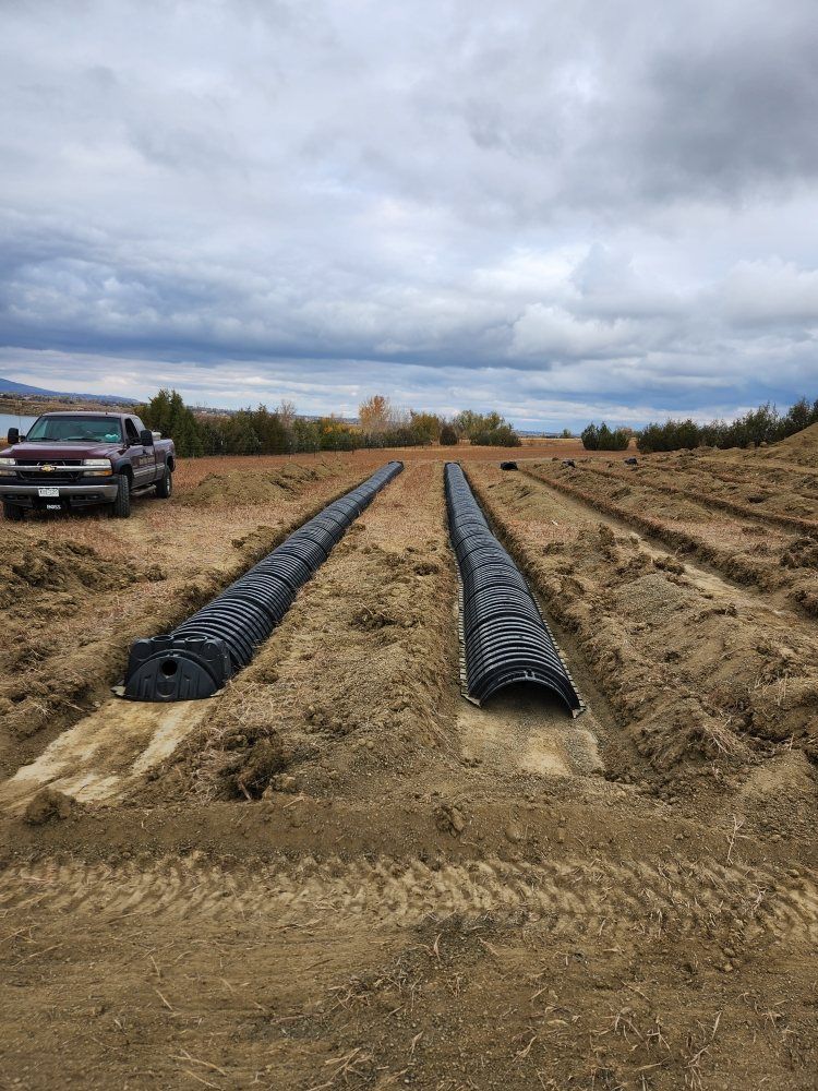 Two long, black drainage systems in parallel trenches, truck in the background, cloudy sky.