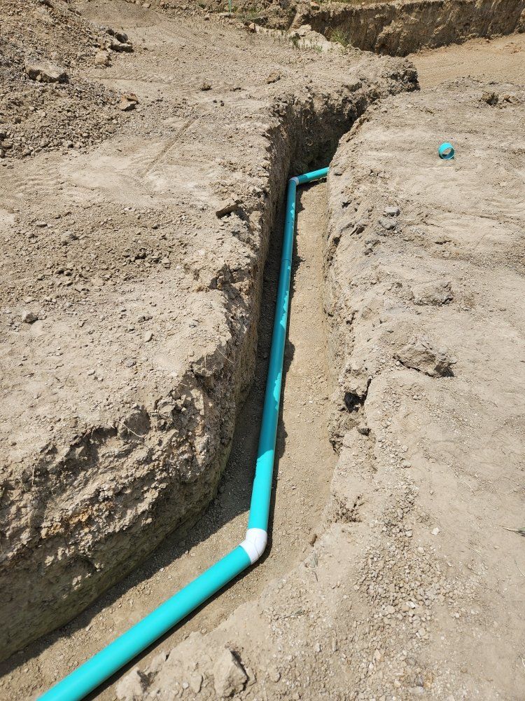 Blue PVC pipe in a trench, likely for plumbing or irrigation, surrounded by dirt.