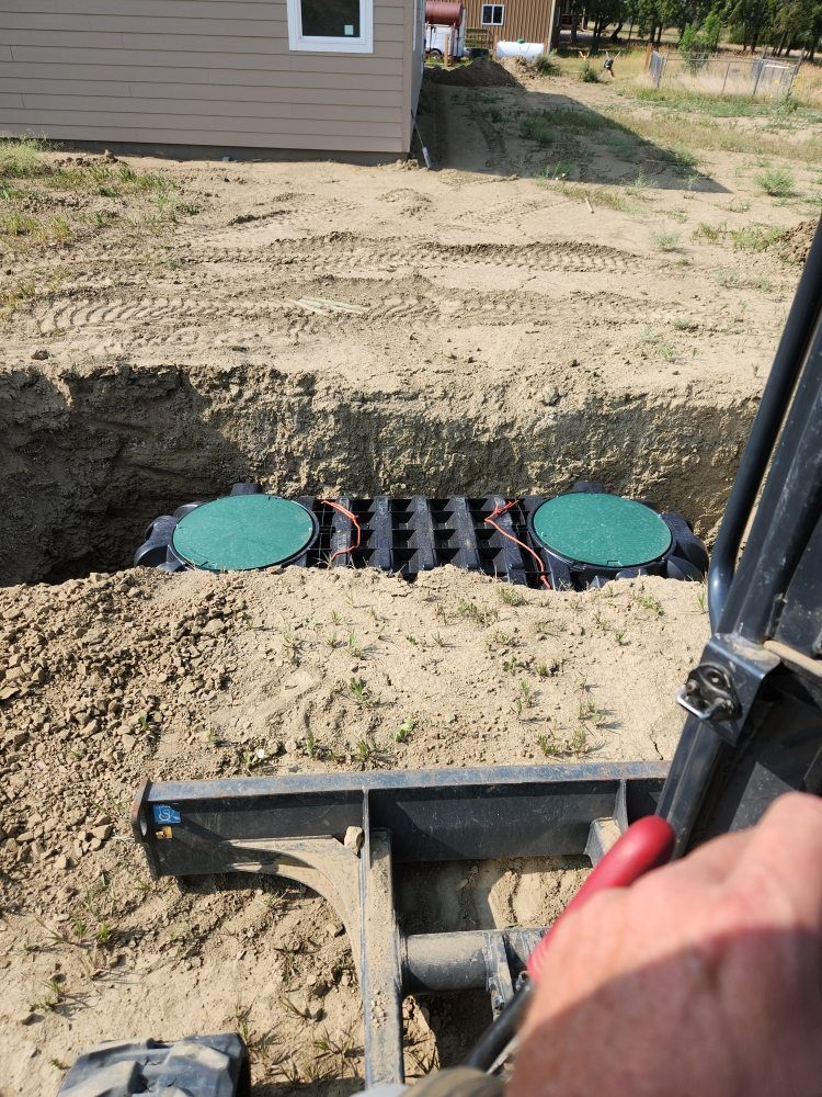 Septic tank installation in progress; excavator with arm near a trench with two green tank lids.