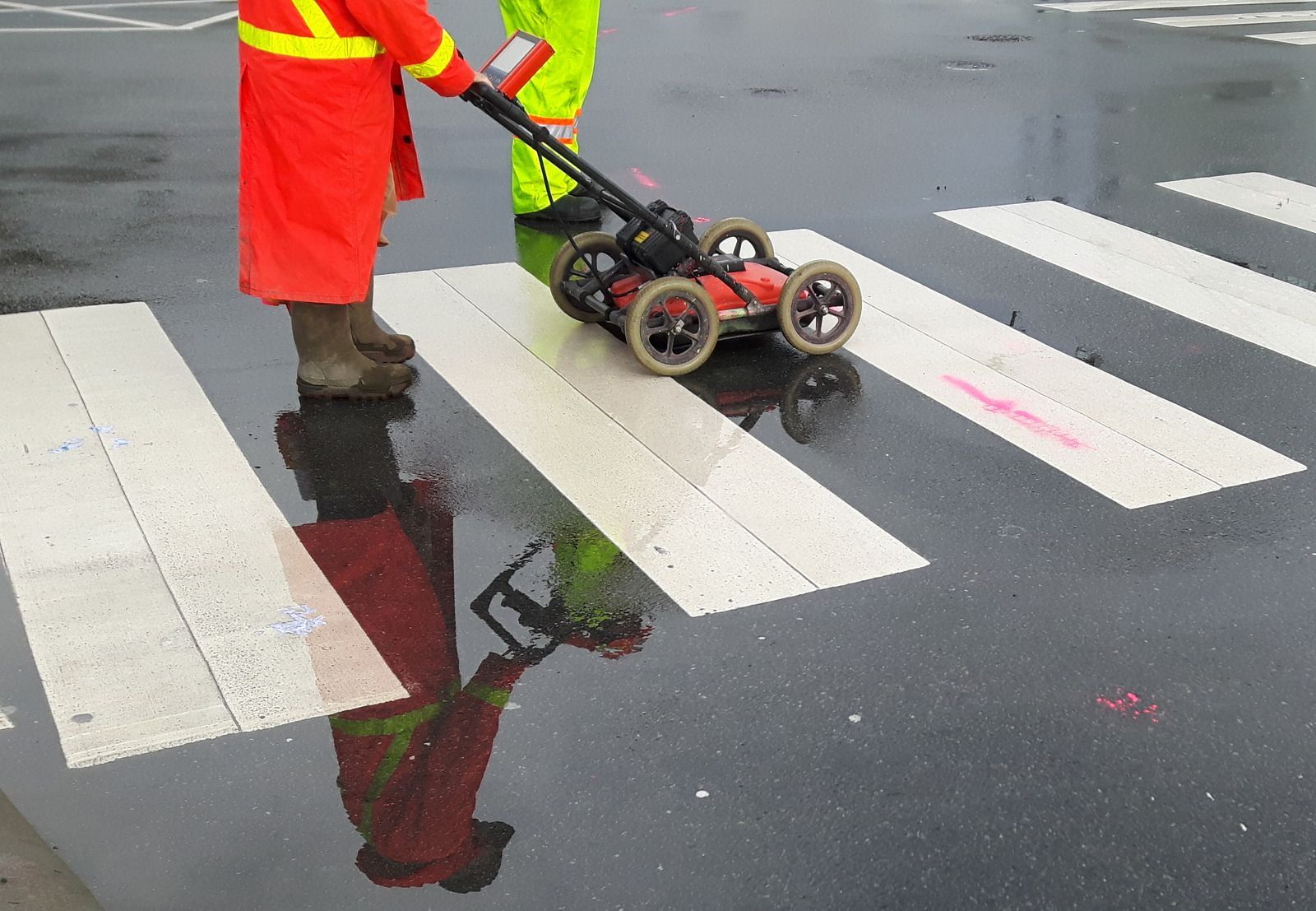 Excavator on freshly tilled soil, next to a concrete basketball court. Houses and  in the distance under a cloudy sky.