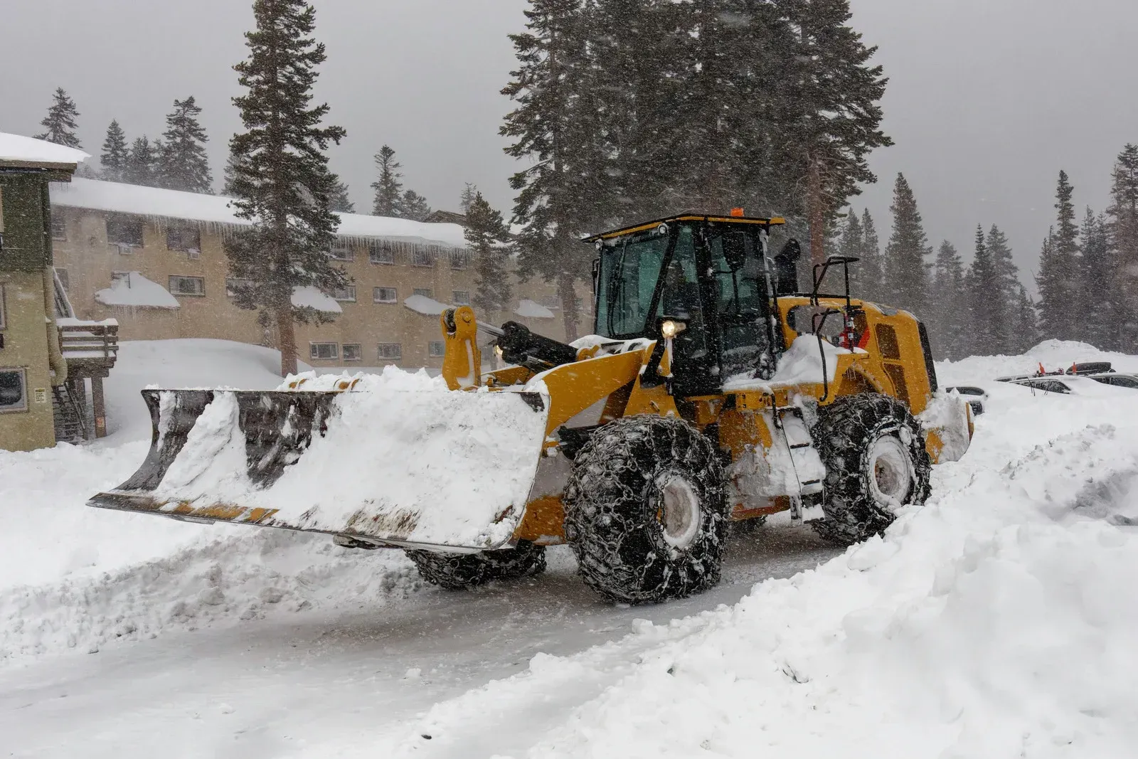 Yellow snowplow clearing snow from a road in a snowy environment.