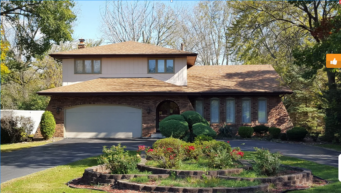A large brick house with a garage and a circular garden in front of it.