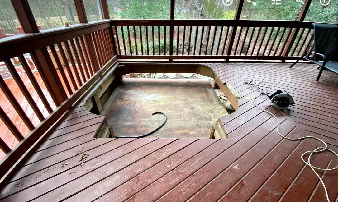An opening in a stained wooden deck on a screened porch, with a circular saw sitting on the boards nearby.