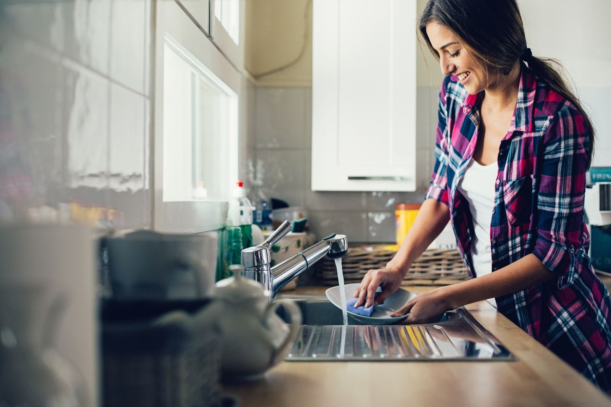 A woman is washing dishes in a kitchen sink.