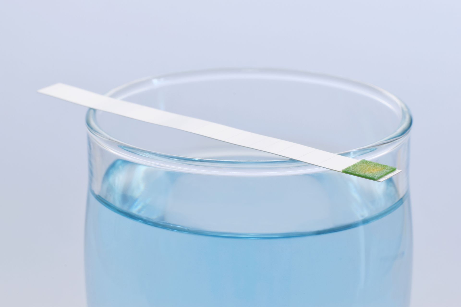 A close up of a glass of water with a hard water testing strip on top.