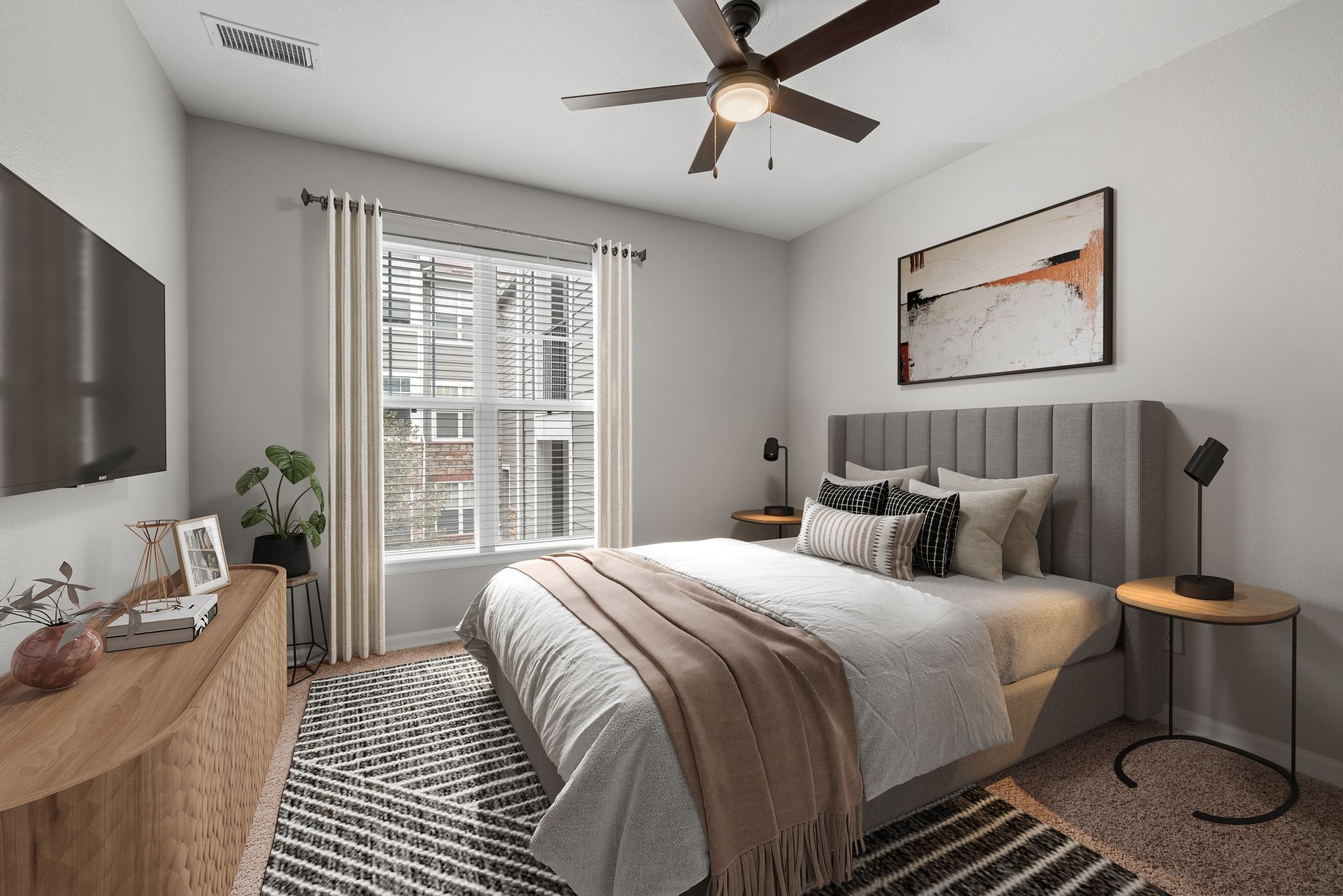 Bedroom with gray upholstered bed, two round nightstands, ceiling fan, large window.