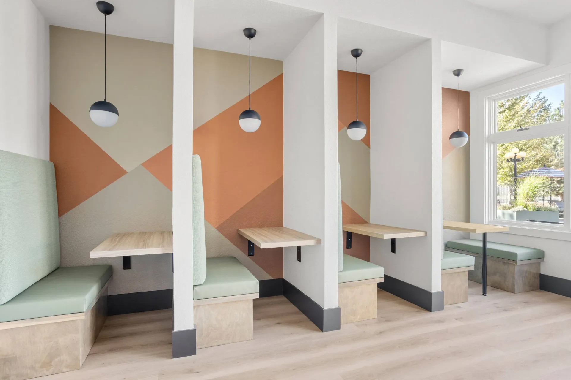 Interior community lounge with partitioned booth seating, pendant lights, and a geometric mural.