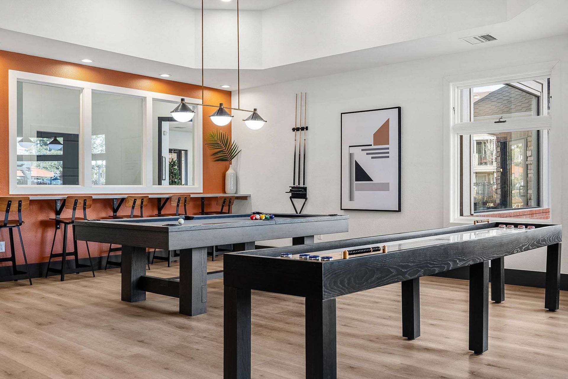 Interior game room with two pool tables, bar seating, warm wood floor, and modern art.