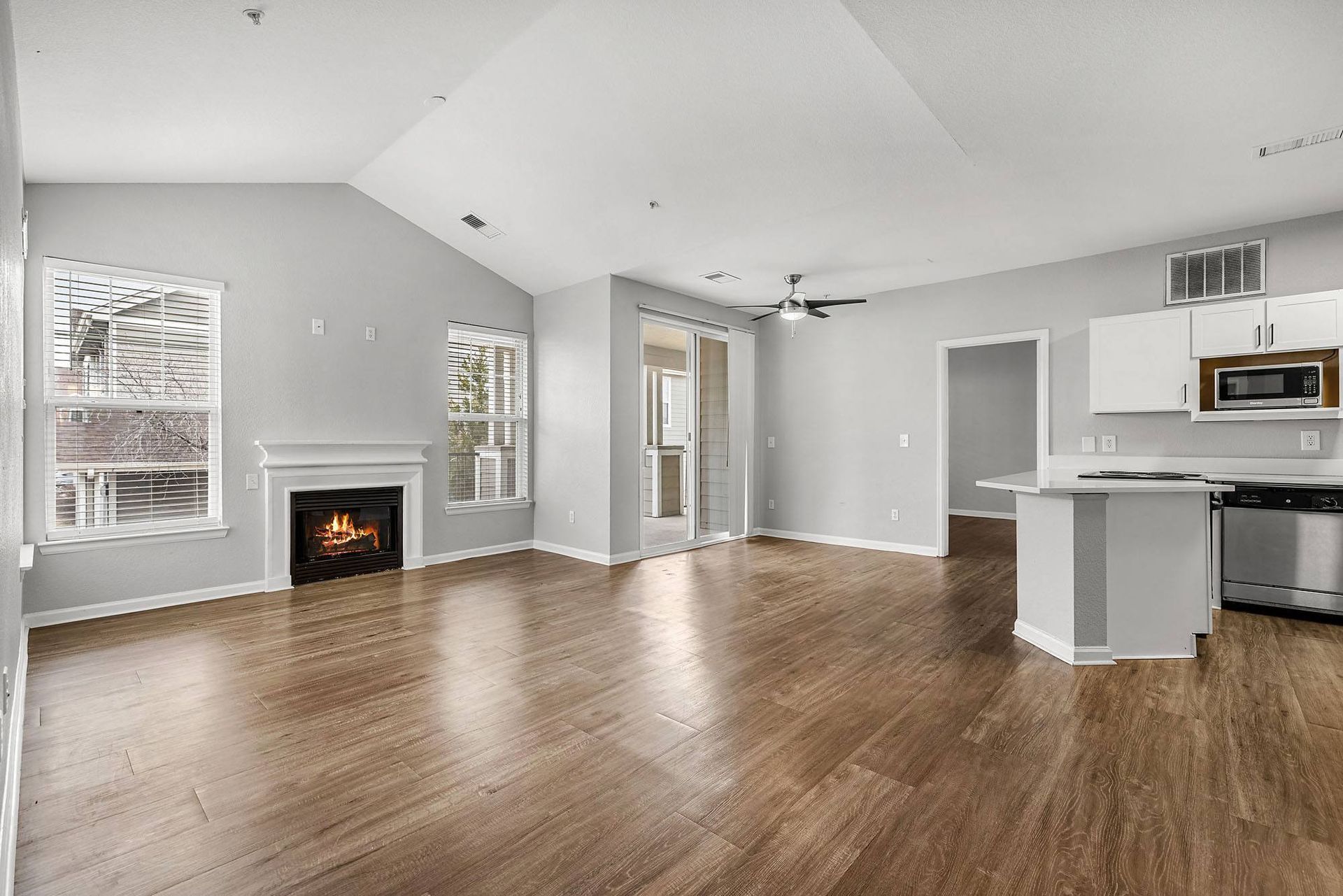 Living room with a gas fireplace, large windows, and an open kitchen in a modern apartment.