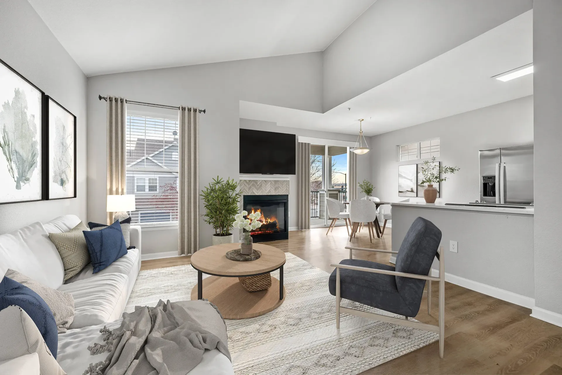 Bright open living area with sofa, fireplace, TV, dining nook, and kitchen island in an apartment.