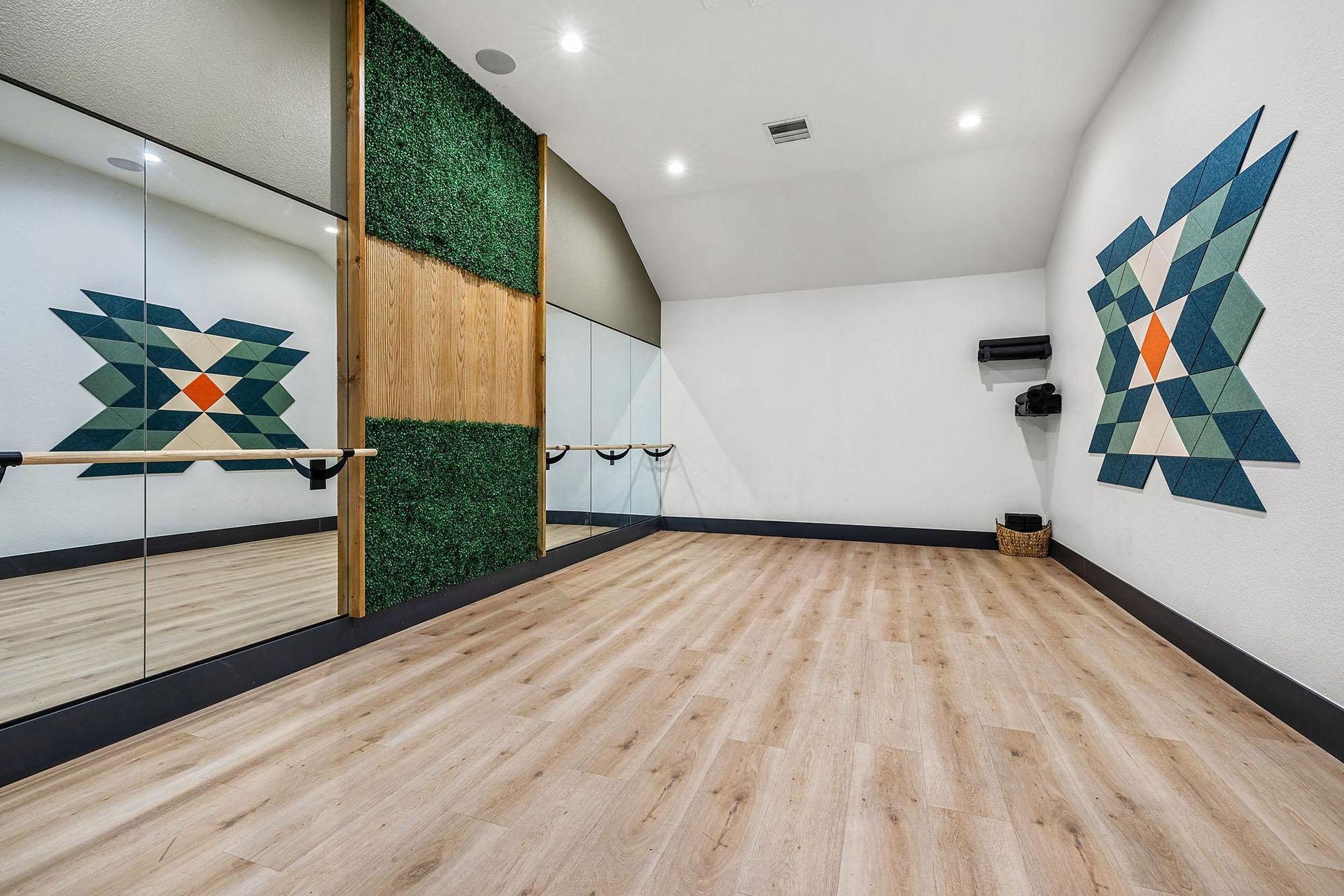 Fitness studio with mirrors along one wall, ballet barre, wood-toned flooring, and geometric wall art.