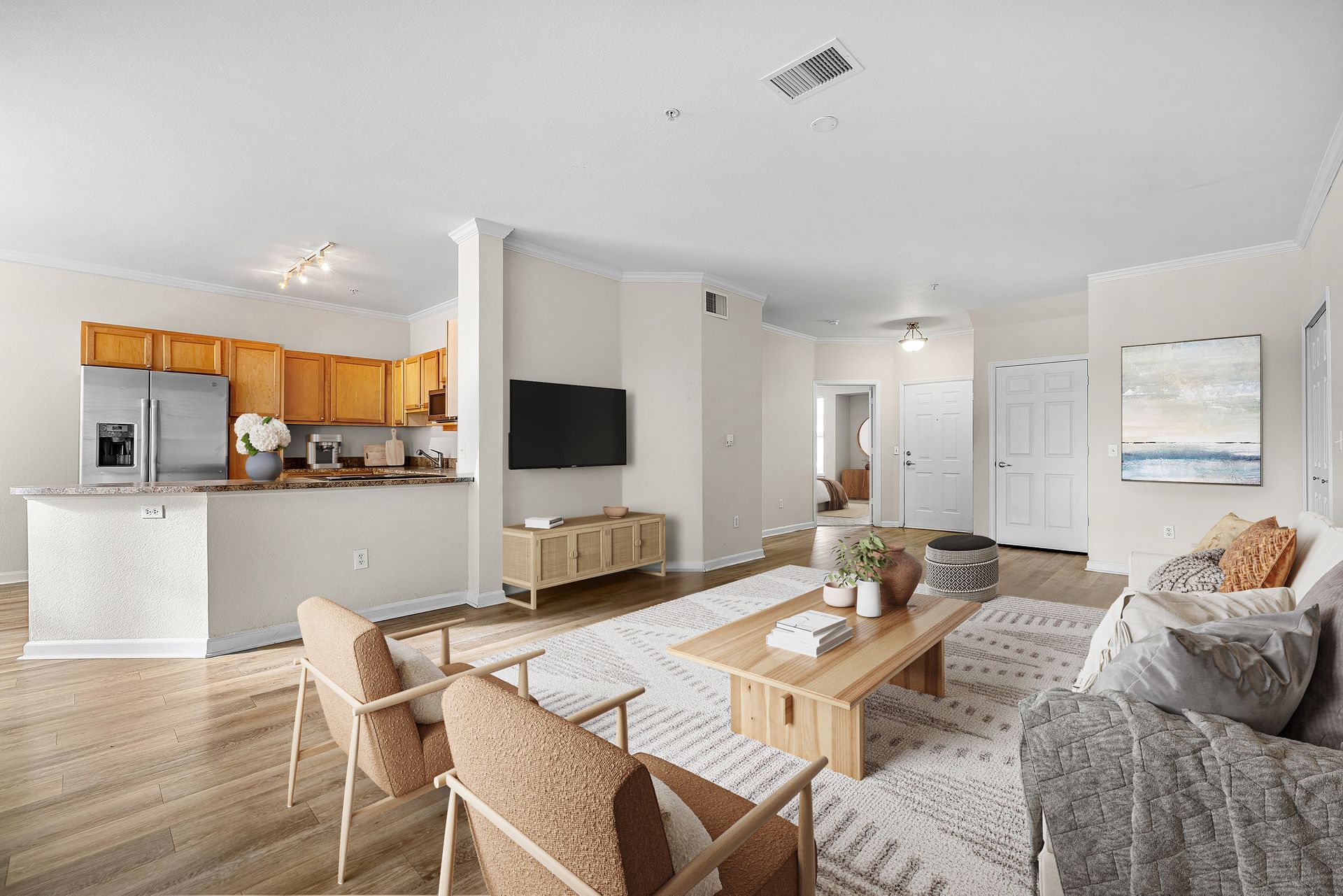 Open-concept living area with kitchen counter, hardwood floors, beige walls, and a wall-mounted TV.