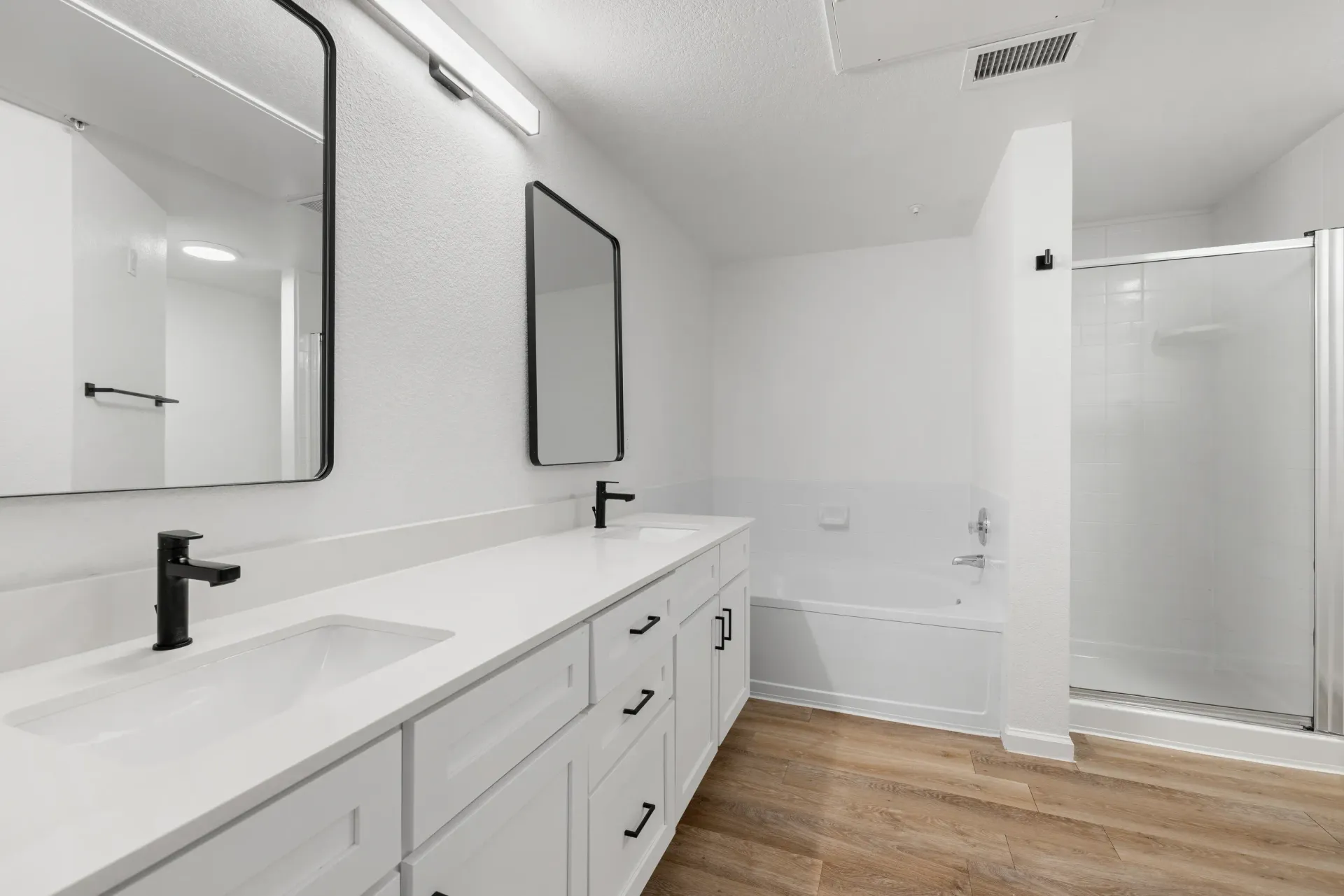 Modern white bathroom with a double-sink vanity and a glass-enclosed shower.