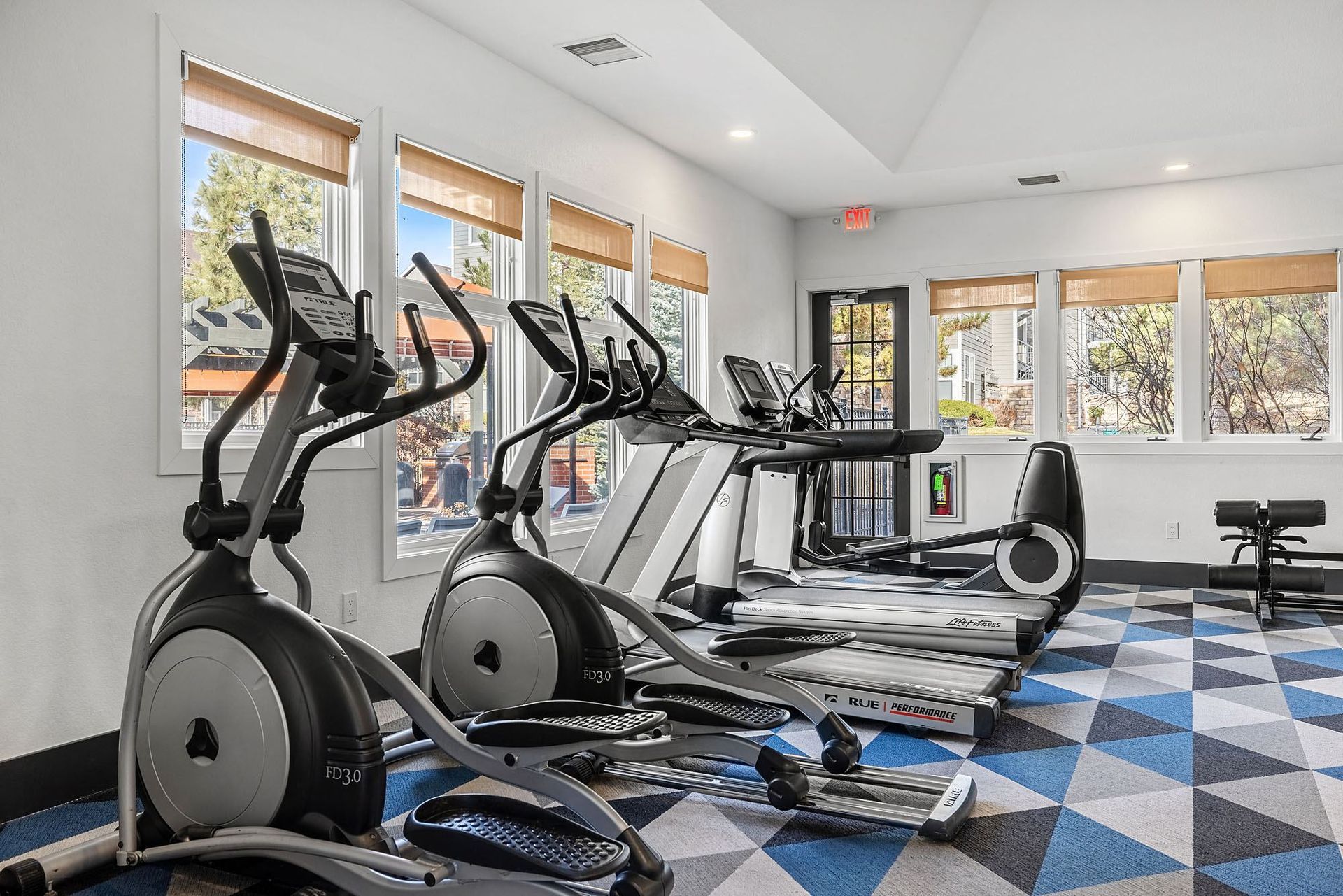 Fitness center with treadmills and elliptical machines by large windows.