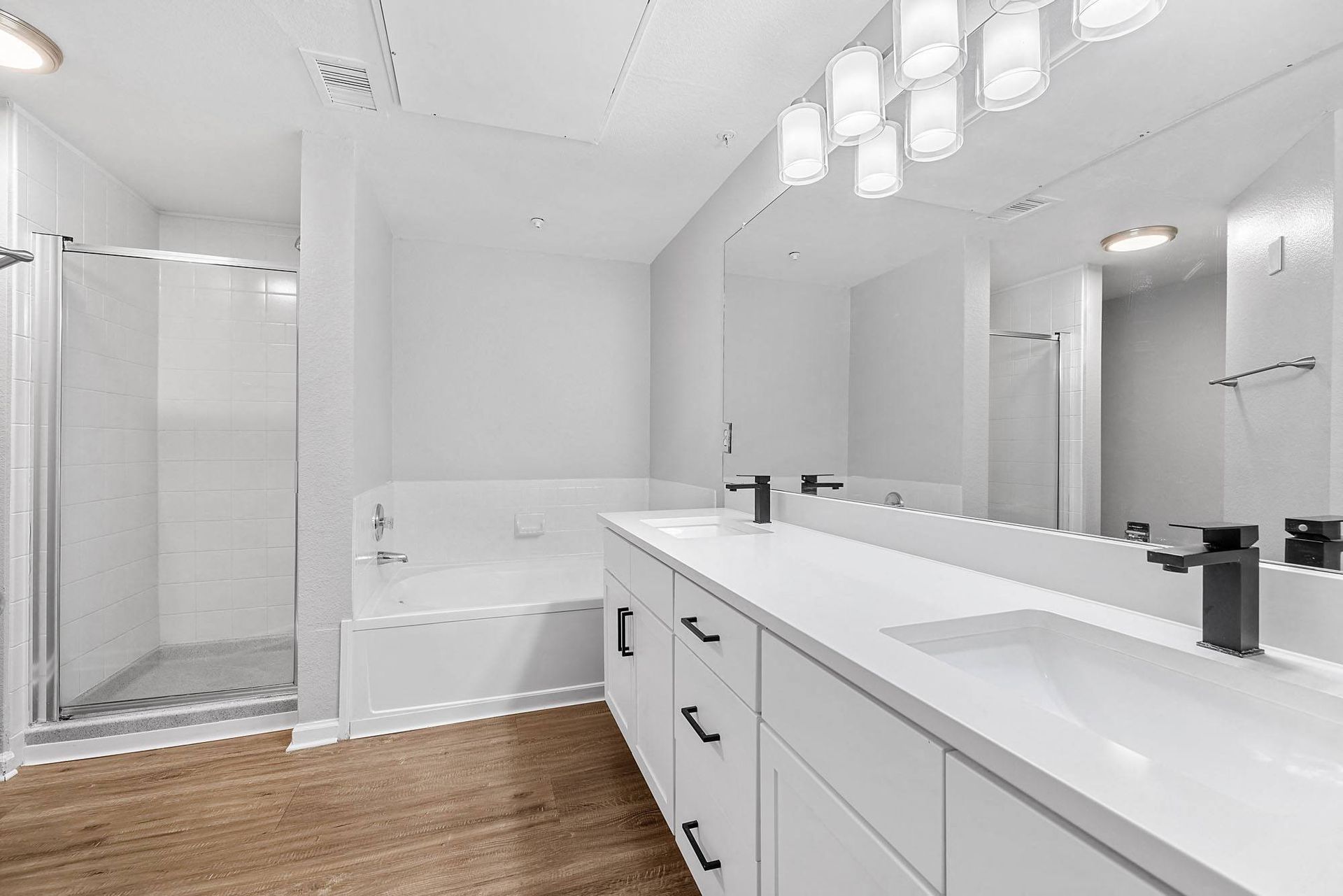 Modern apartment bathroom with double vanity, tub and shower.