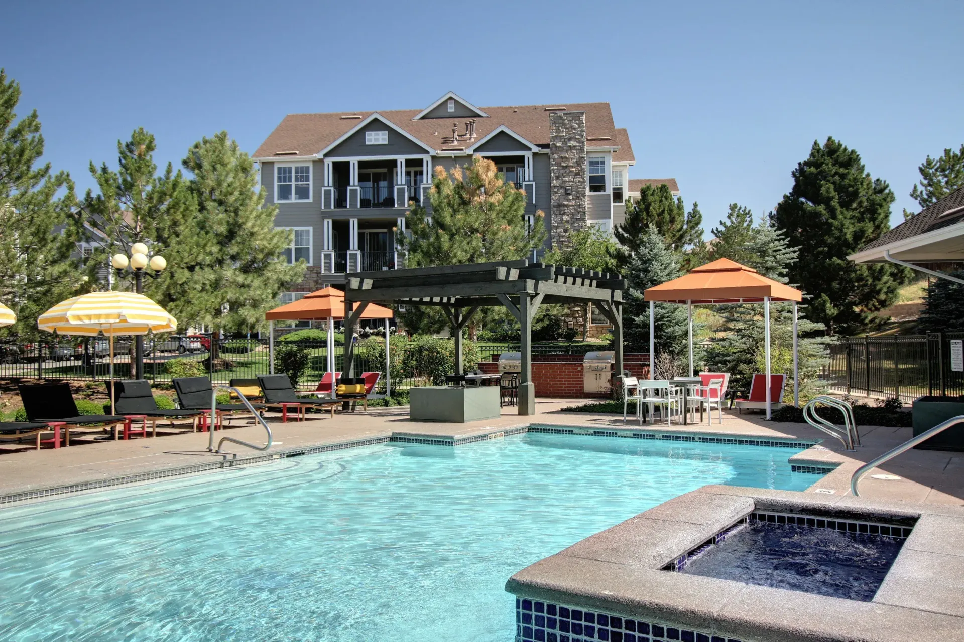 Outdoor pool area with lounge chairs, umbrellas, and a pergola at a residential community.