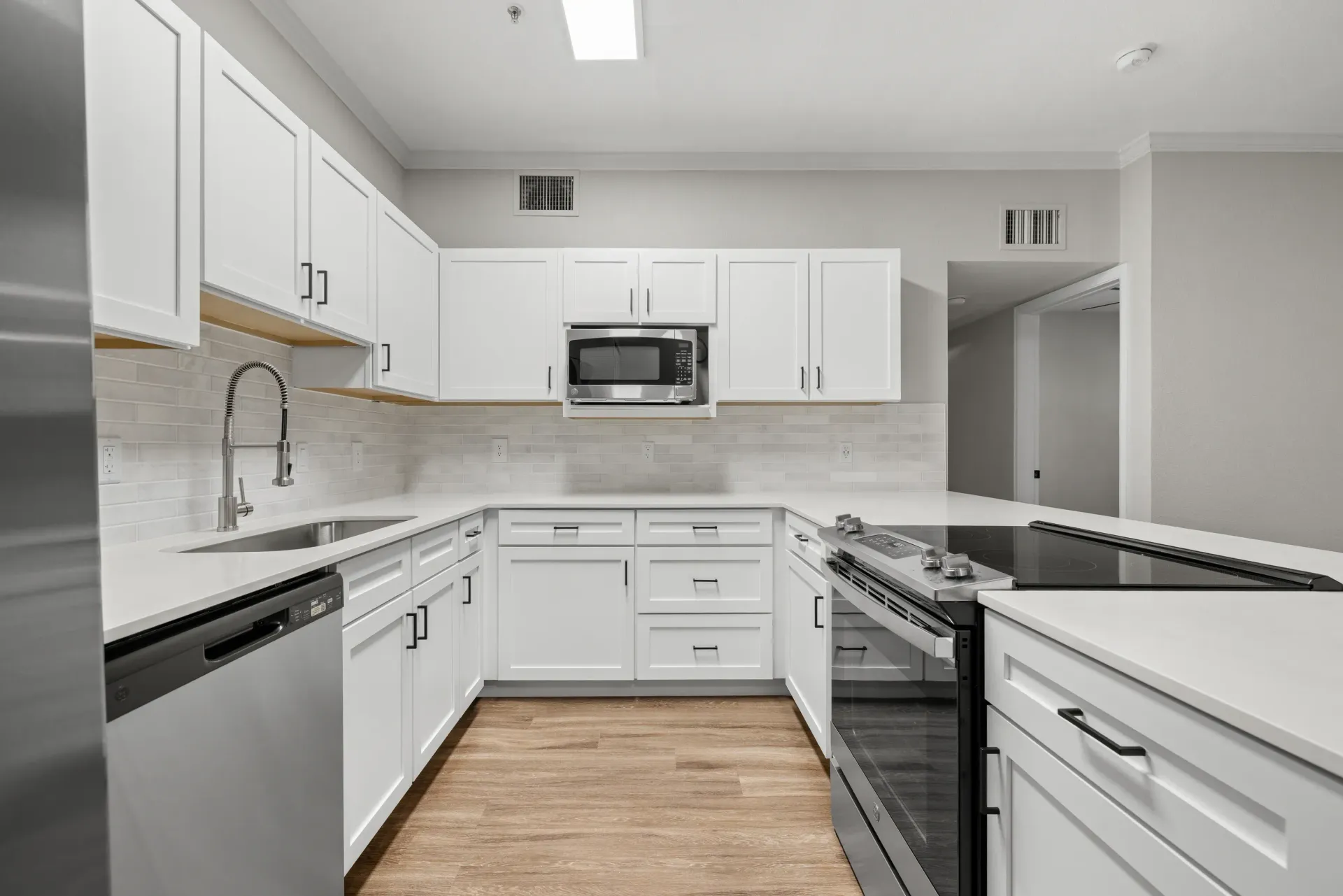 Modern apartment kitchen with white cabinets, stainless steel appliances, and a tile backsplash.