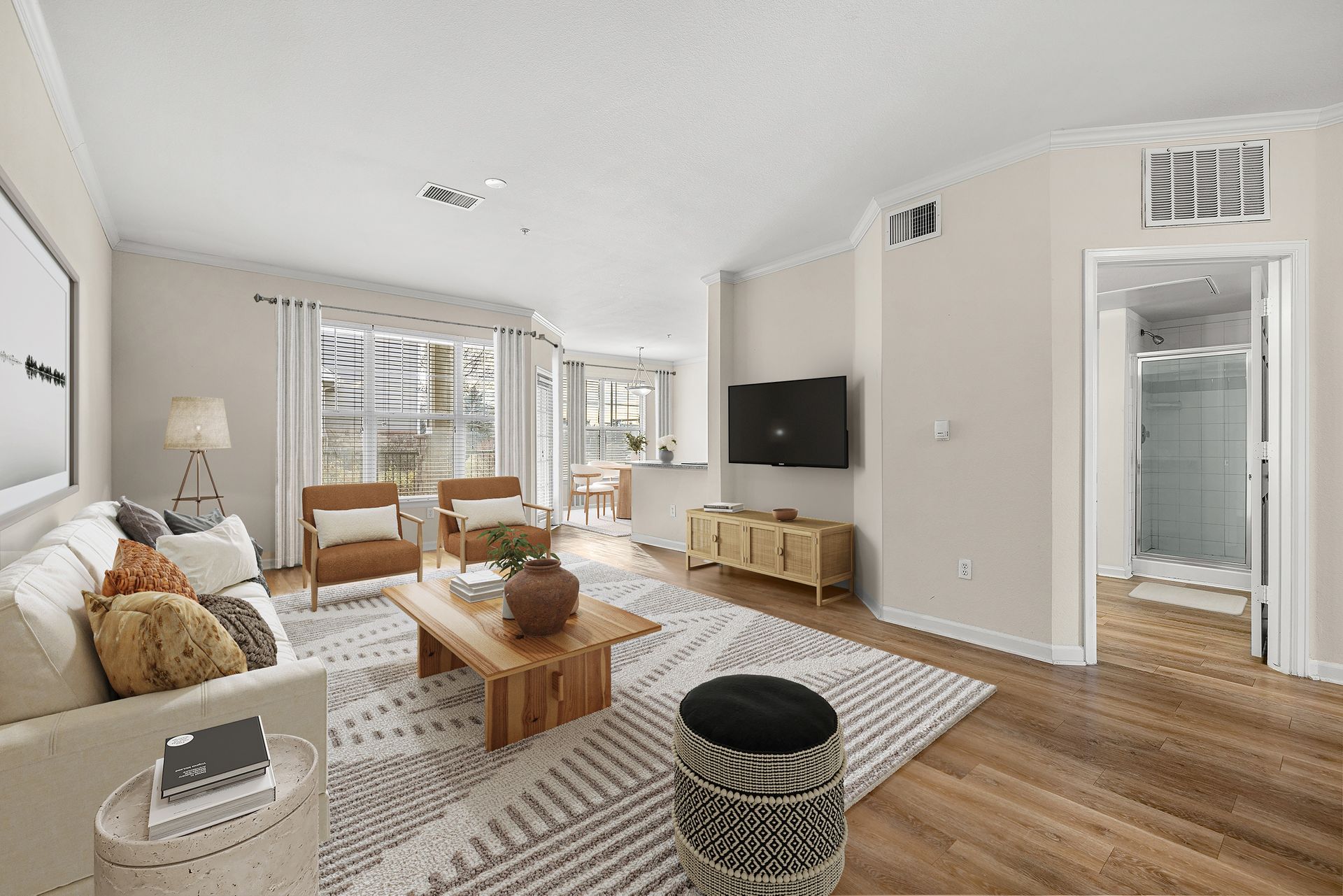 Living room of an apartment with a sofa, two chairs, coffee table, rug, and wall-mounted TV.