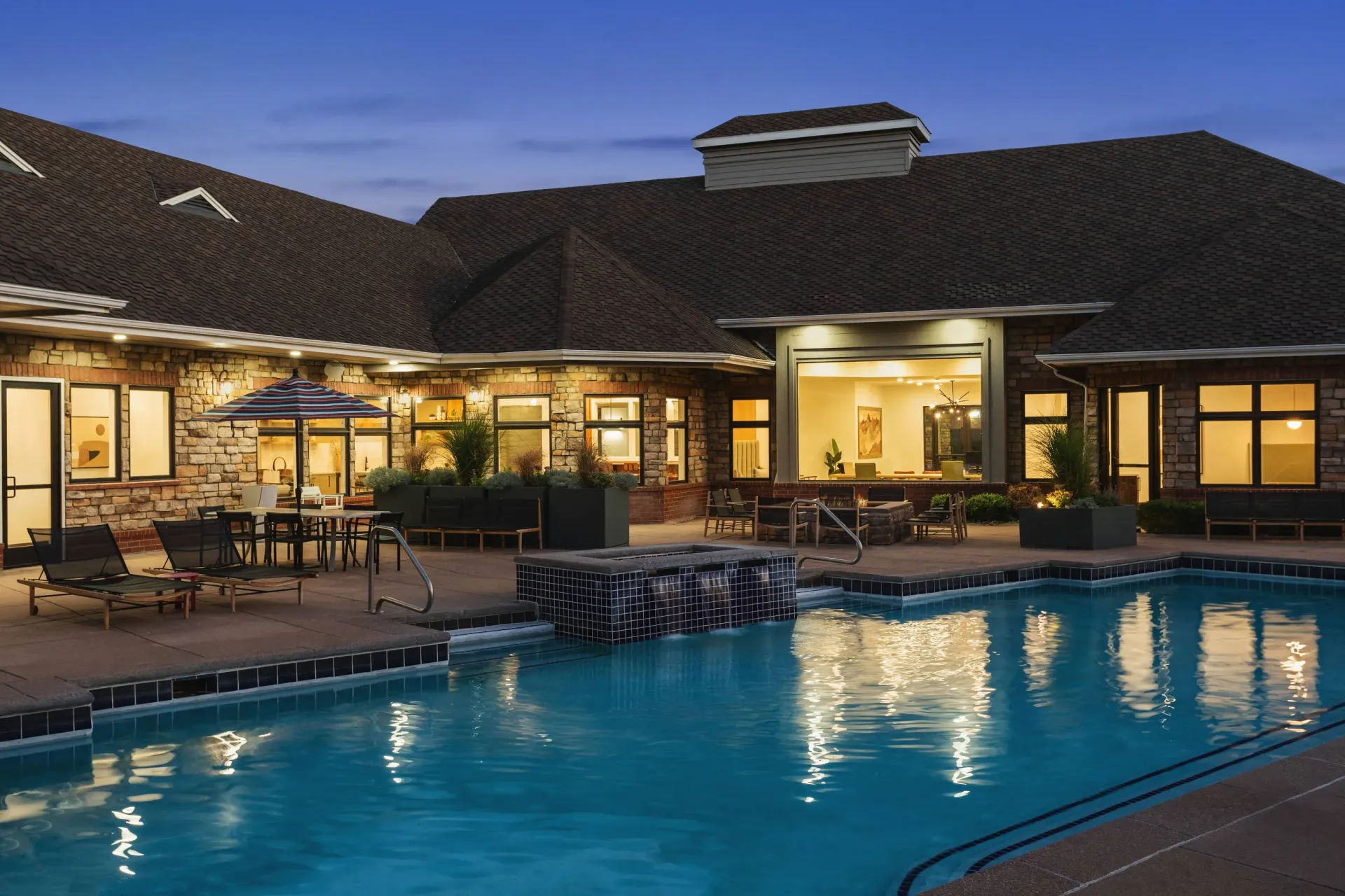 Outdoor pool area at an apartment community with lounge chairs and umbrellas.