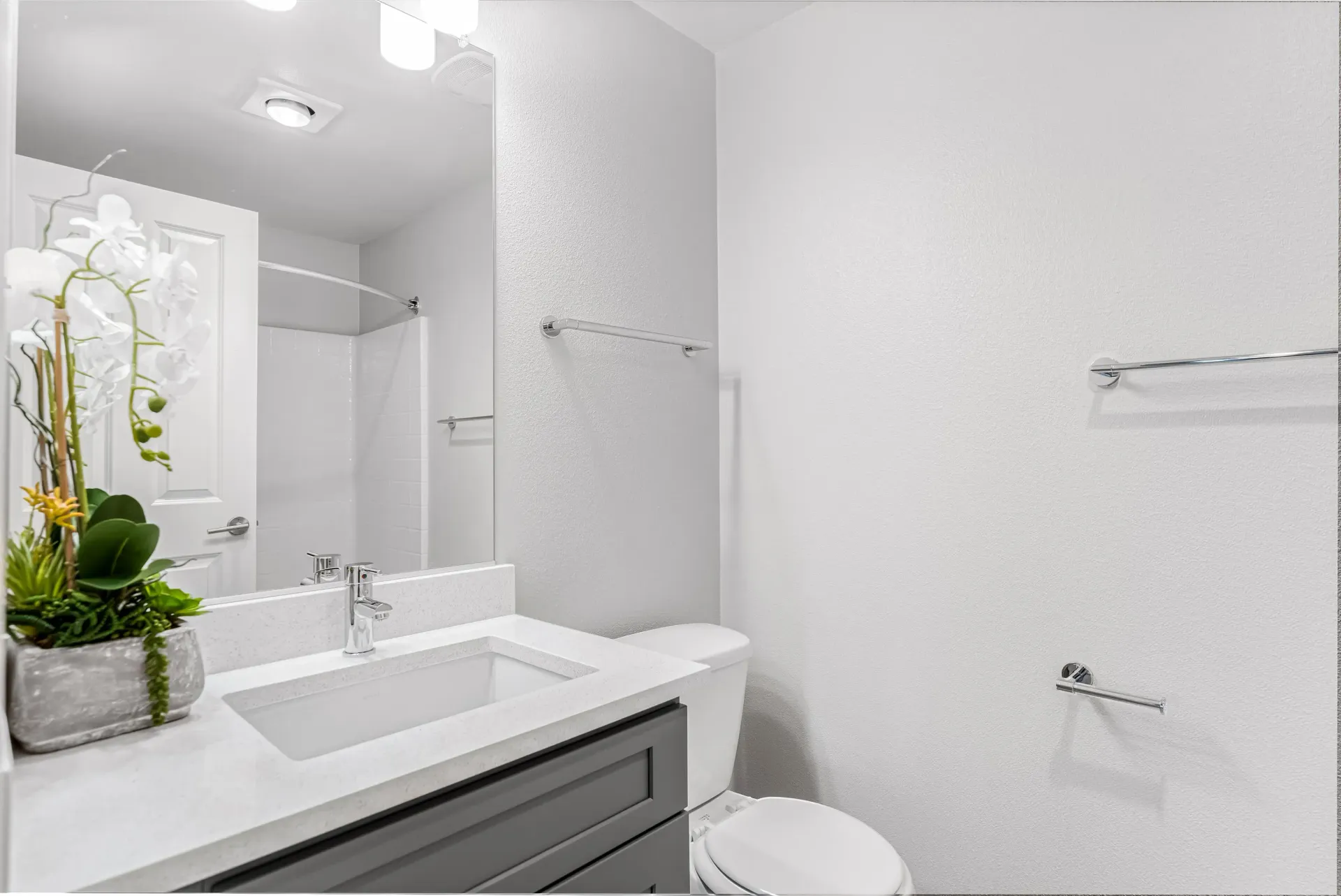 Bright apartment bathroom with vanity sink, large mirror, toilet, and shower-tub in neutral tones.