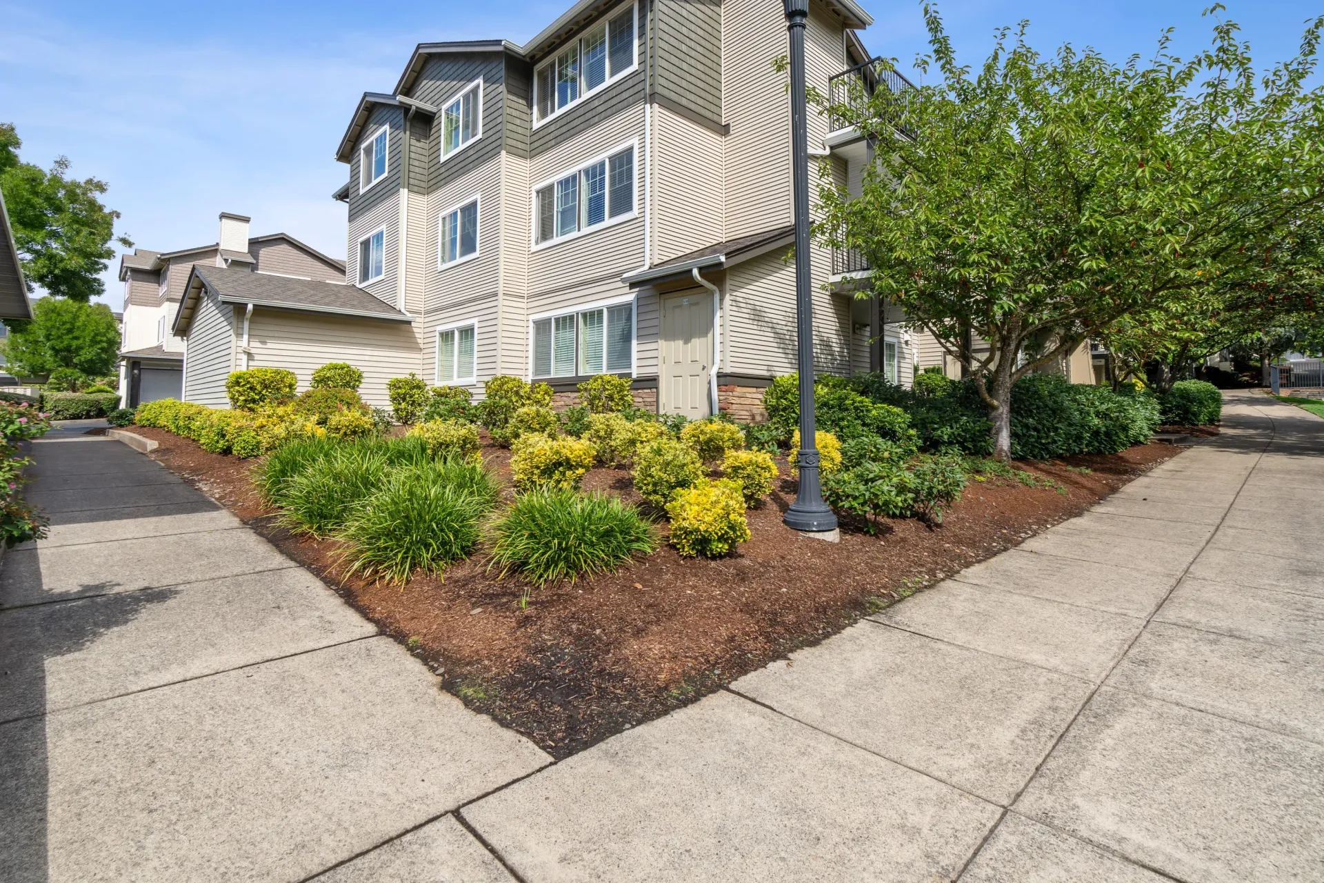 Exterior view of a multi-story apartment building with landscaped front garden and sidewalks.