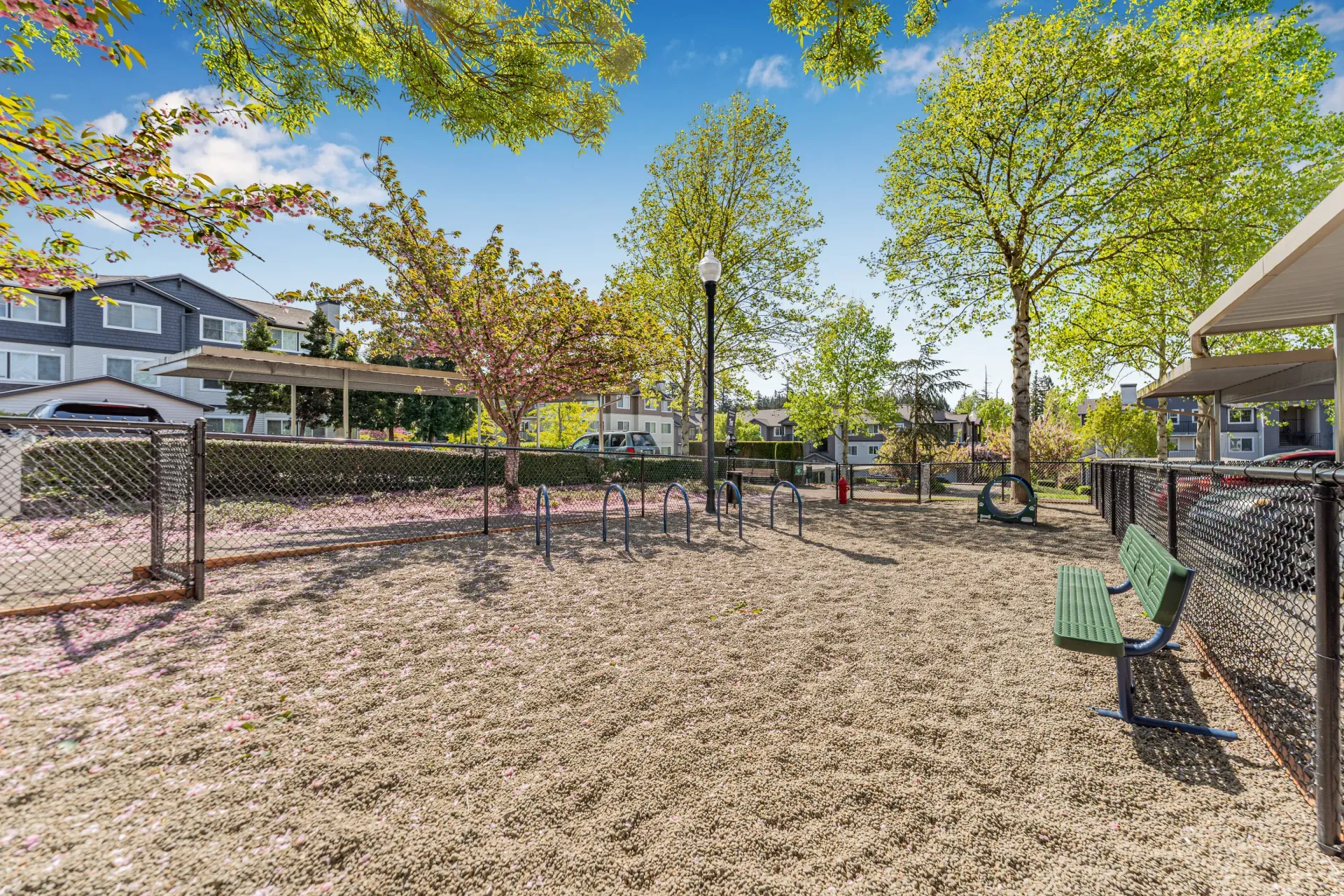 Fenced community playground with metal bars, benches, and trees near apartment buildings.