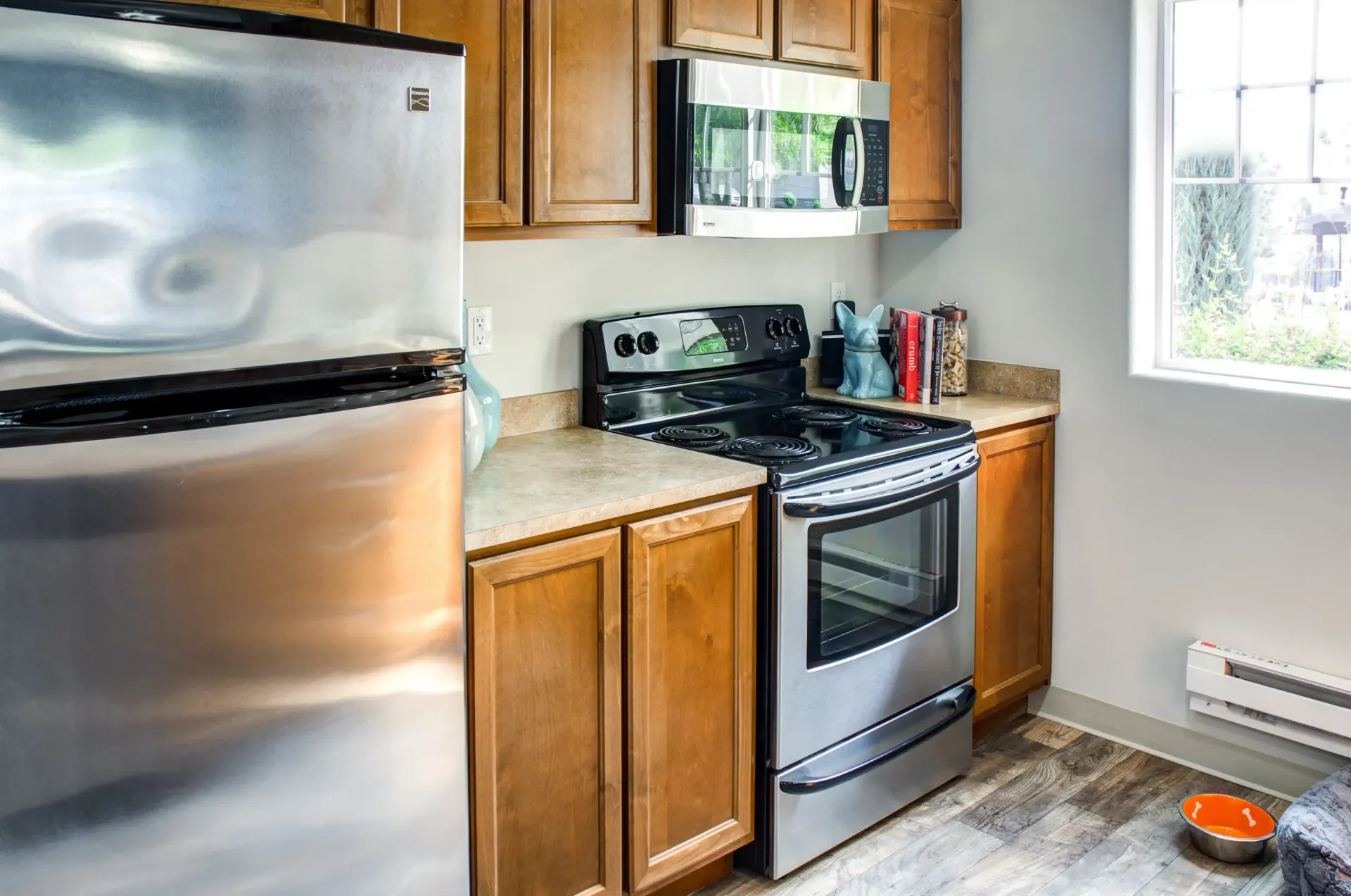 Modern apartment kitchen with stainless steel refrigerator, oven, microwave, and wooden cabinets.