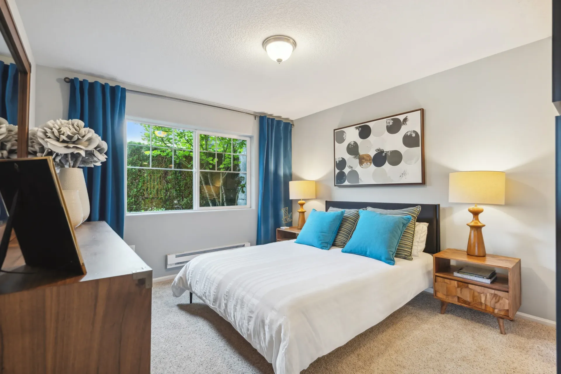 Bedroom in an apartment with a bed, blue curtains, and warm lamps on nightstands.