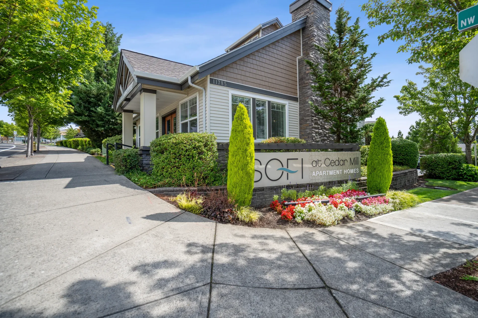 Exterior view of a modern apartment community entrance with a landscaped sign and walkway.